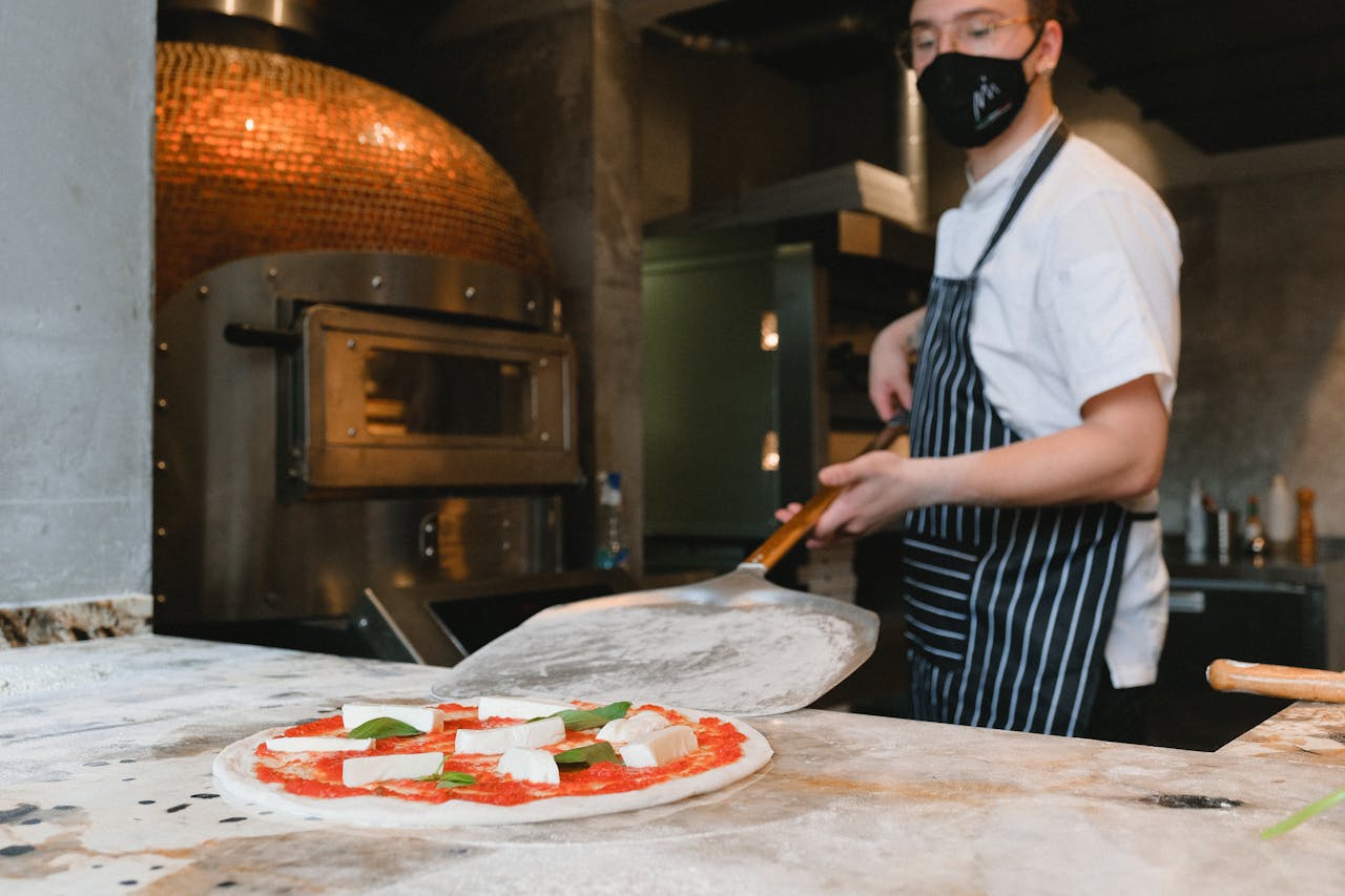 A chef prepares a Neapolitan pizza in a rustic kitchen with a wood-fired oven.